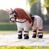 Stuffed pony toy with a pale pink saddle pad on a paved path outdoors